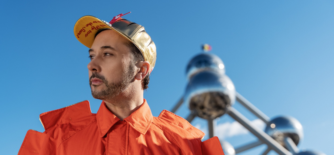 Halve finalist Eurosong Gustaphe met oranje hemd aan, staat voor het atomium